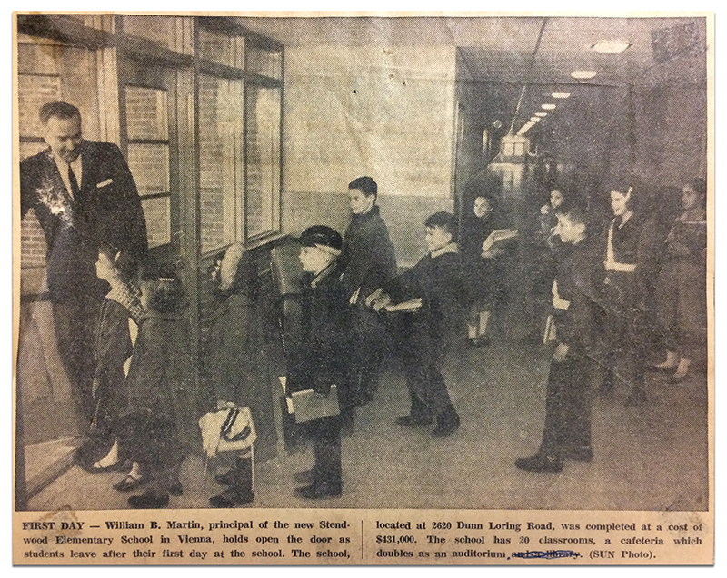Newspaper clipping from February 1964, showing a black and white photograph of Principal William Martin holding open the door as students leave after their first day of school. The caption states that the school is located at 2620 Dunn Loring Road, and was completed at a cost of $431,000. The school has 20 classrooms, and a cafeteria which doubles as an auditorium. 